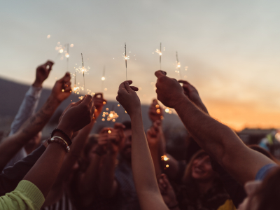 Group of hands held up in air, and all holding lit sparklers.