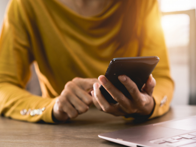 Image of a woman using a mobile phone in front of a laptop