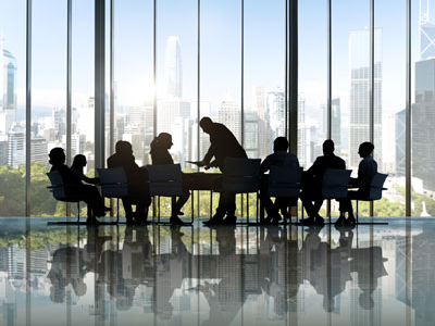 A shilouette of people sitting around a table, with what appears to be a corporate type meeting.