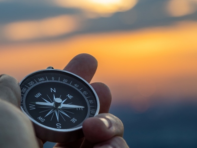 Image of a hand holding a compass with a sunset background
