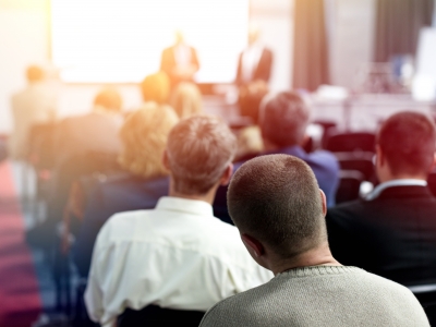 Image of people sitting in rows at an event, watching a presentation