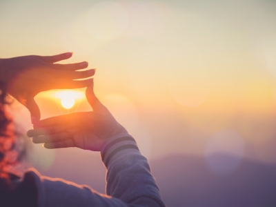 Image of a woman holding her hands up to frame the sunset