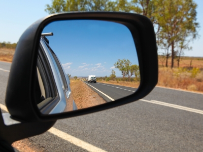 Image of a car side mirror, showing a road and car towing a caravan in central Queensland