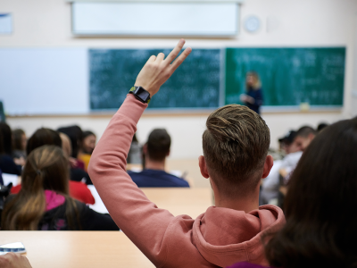 Image of a university classroom where a student has their hand raised.