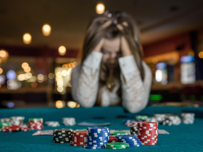 Image of a woman with head in hands at a casino table with gambling chips