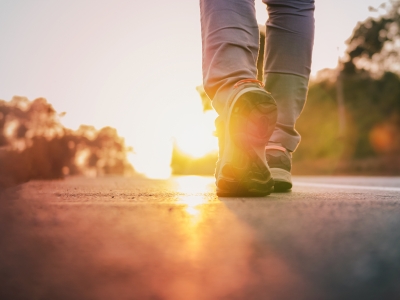 Image of a road landscape with a person's feet and legs in frame, walking away towards the sunrise/sunset.
