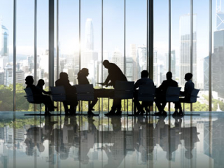 A shilouette of people sitting around a table, with what appears to be a corporate type meeting.