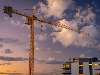 Image of a crane in front of part of an apartment building and sunset