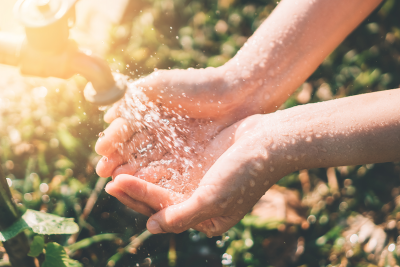 A person cupping water in their hands from a tap outdoors