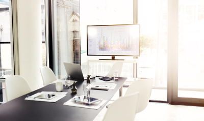 Image of a meeting table with a graph showing on a screen