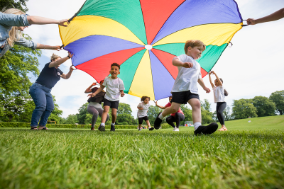 Image of young children running under a colourful parachute playing outdoors