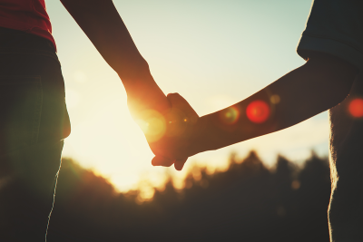 Silhouette of adult and child holding hands with sunrise in background