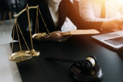 Report thumbnail: 2 people at a desk in front of a computer, with justice scales and gavel on the desk 