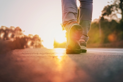 Image of a road landscape with a person's feet and legs in frame, walking away towards the sunrise/sunset.