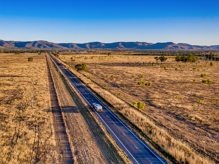 Image looking over a rural landscape with a caravan on the road down the centre and mountains in the distance