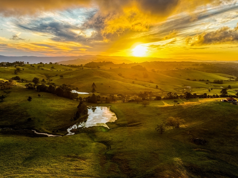 Image of sunrise over rolling green hills and a lake