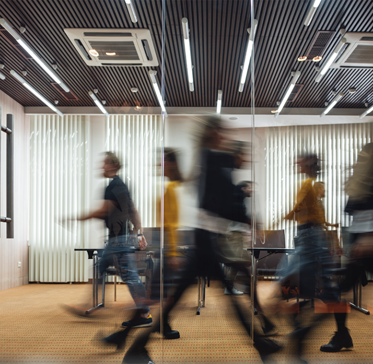 Image of an office with multiple blurred people walking past