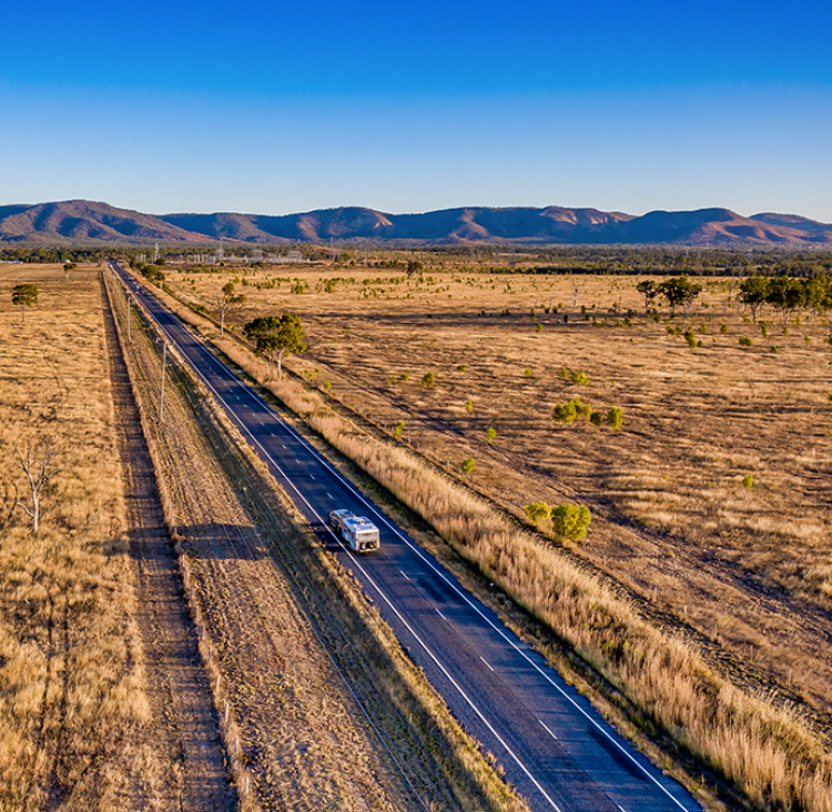 Image looking over a rural landscape with a caravan on the road down the centre and mountains in the distance